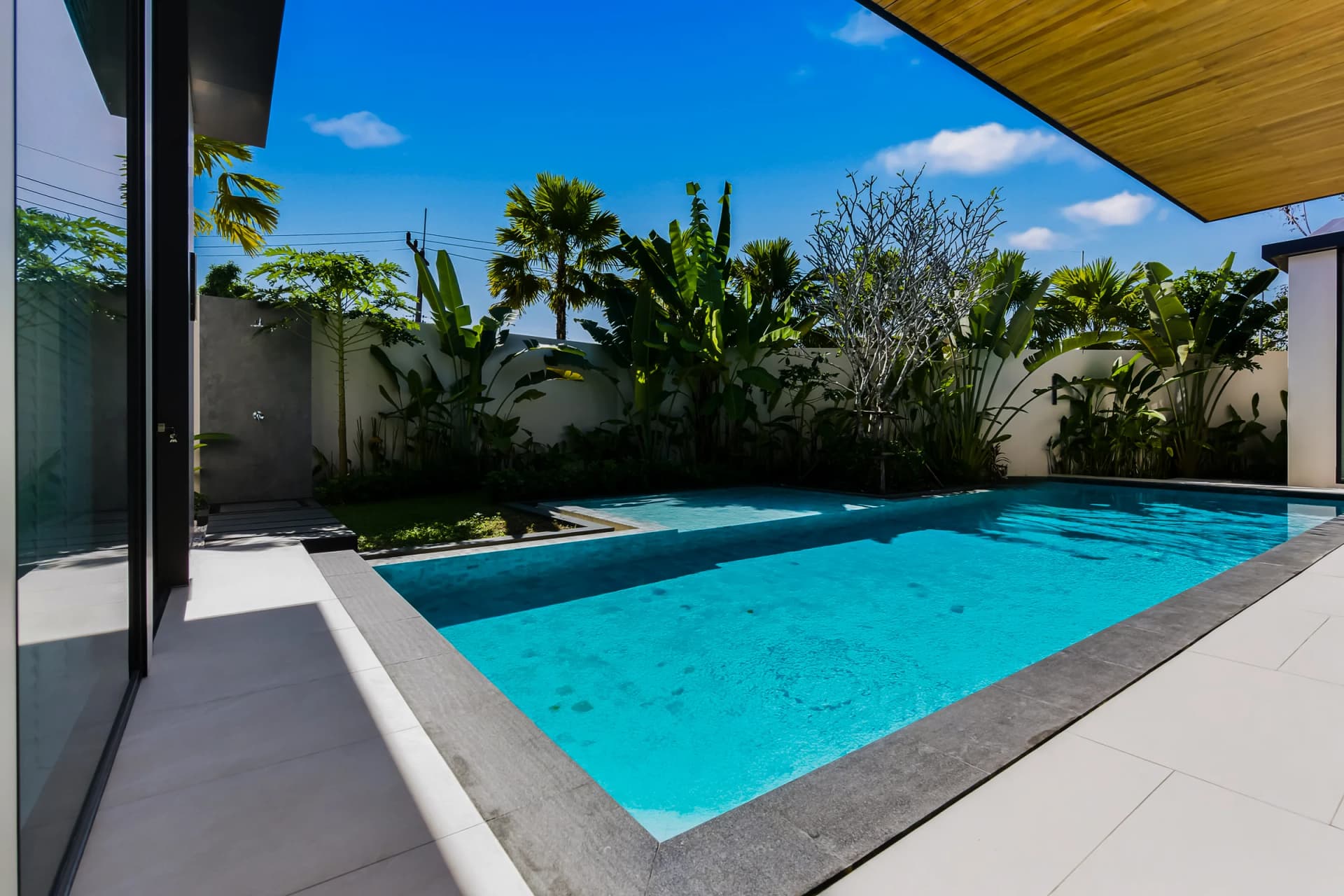 Villa 1: the L-shaped pool and the pale stone deck along the garden wall